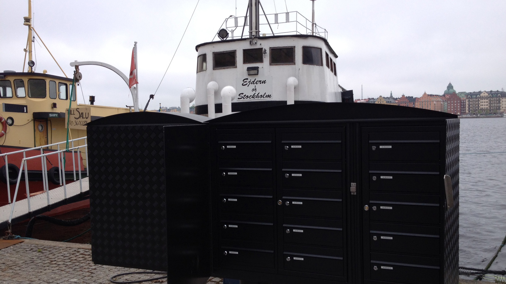 I förgrunden brevlådor vid Söder Mälarstrand. I bakgrunden två förtöjda fartyg.